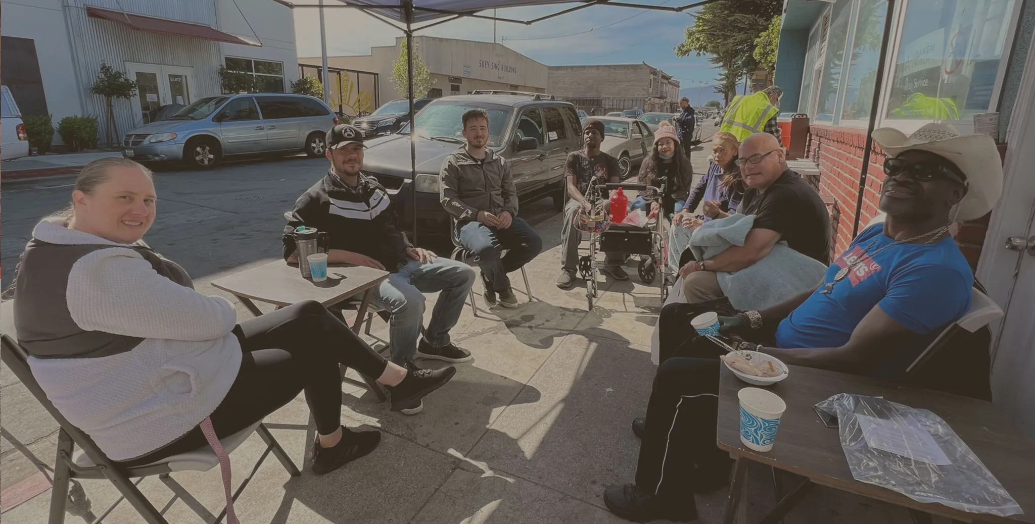 Volunteers and neighbors sharing coffee under a canopy on Soledad Street